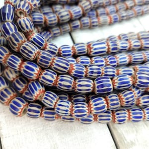 May include: Strands of vintage glass beads. The beads are oval-shaped with a white base, blue stripes, and red accents. The beads are strung together, creating a textured and colorful display. Ideal for jewelry making or crafting.