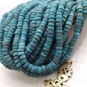 Pode incluir: Um close-up de um fio de contas azuis turquesa. As contas são redondas e têm uma superfície áspera e texturizada. As contas são enfiadas em um fio transparente.