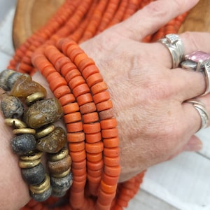 May include: A close-up of a strand of orange beads. The beads are round and have a slightly rough texture. The beads are strung on a cord and are arranged in a circular pattern.