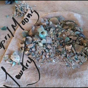 May include: A burlap sack filled with a large pile of broken glass and pottery shards. The shards are various shades of green, brown, and white. The text "April Moon" and "Laundry" is written in black marker on the sack.