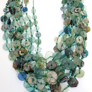 May include: A multi-strand necklace made of green, blue, and brown glass beads. The beads are various sizes and shapes, and some have a frosted or iridescent finish.