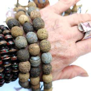 Pode incluir: Um conjunto de três pulseiras de contas com contas marrons, cinzas e pretas. As pulseiras são feitas de materiais naturais e têm um visual rústico.