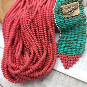 May include: A close-up of two strands of beads. One strand is made of red beads and the other is made of turquoise beads. The turquoise beads are interspersed with silver beads.
