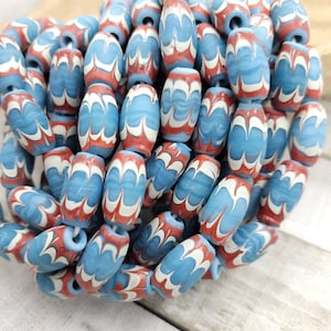 Op de afbeelding: Een close-up van een stapel ovale kralen met een marmerpatroon in blauw, wit en rood.
