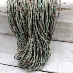 Puede incluir: Una hebra de cuentas turquesa y marrón. Las cuentas son pequeñas y rectangulares, y están enhebradas en un hilo fino. Las cuentas son una mezcla de turquesa claro y oscuro, y tienen una textura ligeramente rugosa.