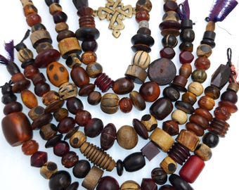 May include: A collection of handcrafted beaded necklaces and pendants in various shades of brown, red, and beige. The beads are made of wood and other materials, with a gold-colored metal pendant in the center. The necklaces are arranged in a fan shape.