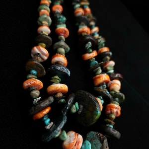 May include: A multi-strand necklace featuring a variety of colorful beads. The necklace includes orange, turquoise, and dark brown beads. The beads are of various shapes and sizes, creating a unique and textured look. The necklace is displayed against a black background.