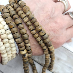 May include: A set of four brown wooden beaded bracelets with black accents. The bracelets are stacked on a person's wrist.
