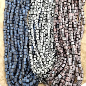 Pode incluir: Três fios de contas de vidro, cada um com um padrão de cor diferente. O primeiro fio é azul e preto, o segundo é branco e preto, e o terceiro é rosa e preto.