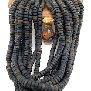 May include: A multi-strand necklace with dark blue, disc-shaped beads. The necklace has a decorative, colourful central bead. The beads are strung together, creating a layered effect. The necklace is displayed against a white background.