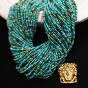 May include: A long strand of turquoise beads with a gold pendant featuring a stylized human face. The beads are a mix of blue, green, and brown colors.