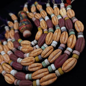 May include: A selection of colourful, handcrafted beads in shades of tan, burgundy, and pastel hues. The beads are strung together, forming a circular pattern. A small, decorative vase with a multi-coloured design is also present.
