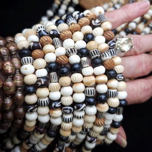 May include: A close-up of a collection of wooden beads in various shades of brown, white, and black. The beads have different patterns and textures, including stripes, swirls, and smooth surfaces.