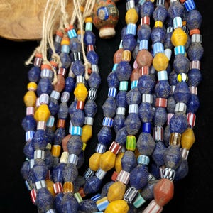 May include: A multi-strand necklace made of blue, yellow, red, white, and green glass beads. The necklace is made of several strands of beads, and the beads are of various shapes and sizes.