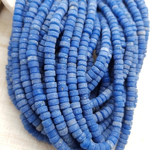 Pode incluir: Um fio de contas de vidro azul com uma superfície texturizada. As contas são pequenas e redondas, e são enfiadas em um fio transparente.