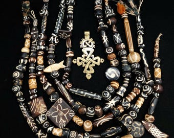 May include: A collection of multiple strands of dark brown and cream-colored patterned beads, featuring various shapes including cylinders, spheres, squares, and fish-shaped pendants, centered around a single ornate brass cross pendant.