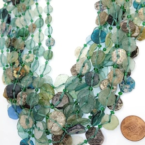 May include: A multi-strand necklace made of green, blue, and clear glass beads. The beads are various shapes and sizes, and some have a weathered look. The necklace is about 18 inches long and is shown next to a US penny for scale.