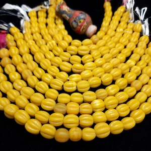 Pode incluir: Um fio de contas de vidro amarelo com textura estriada. As contas são de forma oval e estão dispostas em forma de leque.