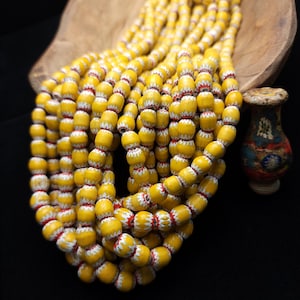 May include: A strand of yellow glass beads with white and red painted designs. The beads are round and have a slightly irregular shape.