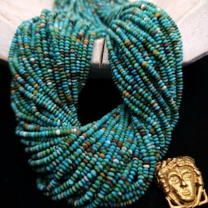 May include: A strand of turquoise beads with a gold pendant featuring a stylized face. The beads are a mix of blue, green, and brown colors.