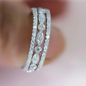May include: A silver band ring with three rows of pave set diamonds. The diamonds are in a delicate, oval shape and are set in a continuous line around the band.