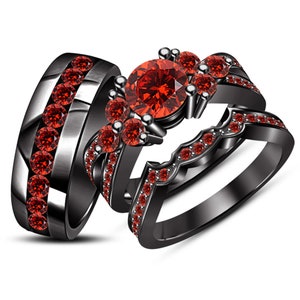 May include: Three-piece black wedding ring set with red gemstones. The set includes a band with a row of stones, a ring with a large center stone and smaller surrounding stones, and a curved band with a row of stones.