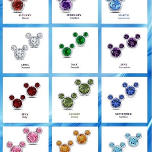 May include: A set of 12 pairs of Mickey Mouse-shaped earrings, each pair featuring a different birthstone. The earrings are arranged in a grid, with each month's birthstone displayed below the corresponding pair of earrings. The birthstones are: Garnet, Amethyst, Aquamarine, Diamond, Emerald, Alexandrite, Ruby, Peridot, Sapphire, Tourmaline, Topaz, and Tanzanite.