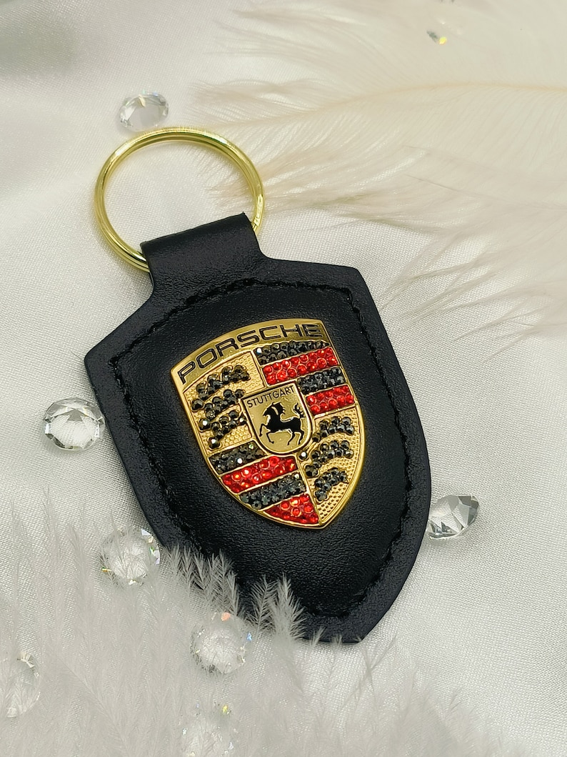 May include: Black leather keychain with a gold Porsche logo featuring red and black rhinestones. The logo says "Porsche" and "Stuttgart".
