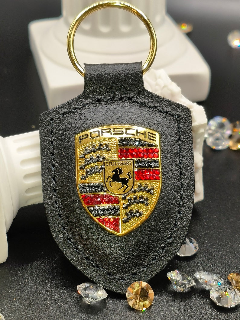 May include: Black leather keychain with a gold Porsche logo featuring red and black rhinestones. The logo says "PORSCHE" and "STUTTGART".