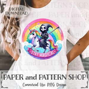 May include: A white t-shirt with a colorful graphic of a Grim Reaper riding a unicorn with a rainbow background. The text "Stay Magical" is written on a pink ribbon.
