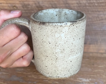 May include: A speckled beige ceramic mug with a rounded handle.