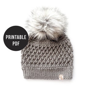 May include: Gray crocheted beanie with a fluffy white pom pom. The beanie has a textured stitch pattern and a small brown label with the text "S2" on the side. Printable PDF.