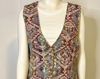 May include: A sleeveless vest featuring a multi-colored geometric tapestry pattern in shades of brown, pink, teal, and cream. The vest has a deep V-neckline, a three-button front closure, and a pointed hemline, worn over a plain white tank top.