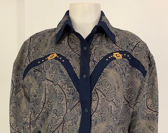May include: A long-sleeved button-down shirt featuring a dark blue and beige paisley pattern. The shirt includes a solid dark blue collar, front placket, and cuffs, with decorative yellow geometric accents on the chest yoke.