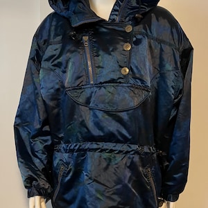 May include: A dark blue hooded jacket with a shiny, iridescent finish. The jacket features a zipper closure, gold-colored buttons, and a drawstring at the waist. The jacket has a front pocket and a high collar.