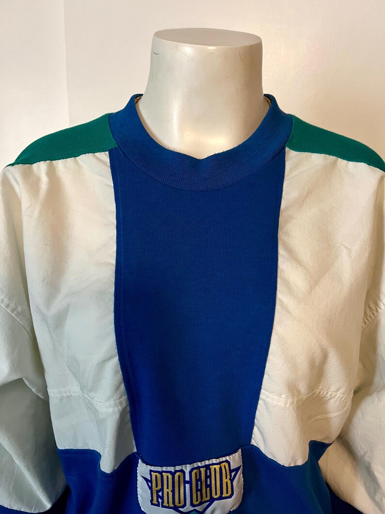 May include: A color-blocked sweatshirt in white, blue, and green. The top features a ribbed blue center panel, white side panels, and green shoulder accents. The lower portion of the shirt has a "PRO CLUB" logo.