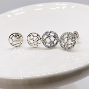Peut inclure: Une paire de boucles d'oreilles en argent en forme de ballon de football. Une boucle d'oreille a un design plein avec des pierres claires, tandis que l'autre a un design creux.