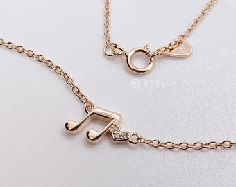 May include: A rose gold-toned necklace featuring a musical note pendant accented with a small heart shape containing three tiny clear stones. The chain includes a round spring ring clasp and a small metal tag stamped with the text STELLA POSH.