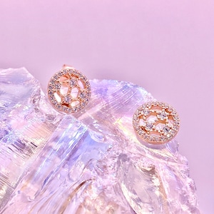Peut inclure: Une paire de boucles d'oreilles en or rose avec un design circulaire pr&eacute;sentant un motif g&eacute;om&eacute;trique de petites pierres de zircone cubique transparentes.