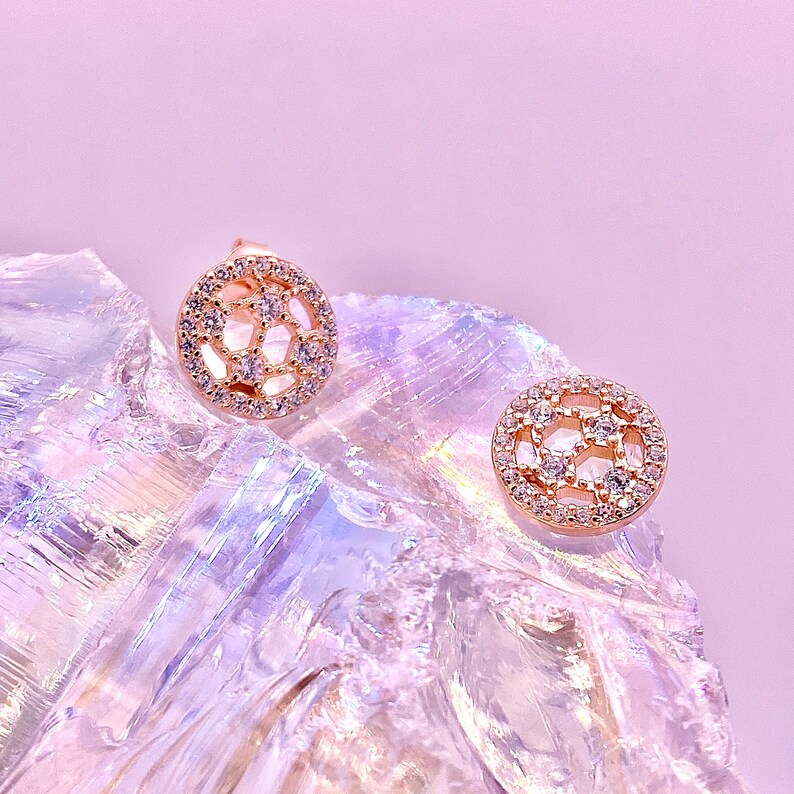 Peut inclure: Une paire de boucles d'oreilles en or rose avec un design circulaire pr&eacute;sentant un motif g&eacute;om&eacute;trique de petites pierres de zircone cubique transparentes.