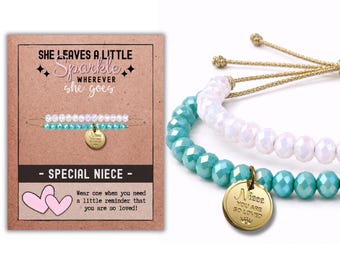 May include: Two beaded bracelets with adjustable gold-tone cords. One bracelet features iridescent white beads, and the other features turquoise beads with a round gold-tone charm engraved with the text Niece YOU ARE SO LOVED.