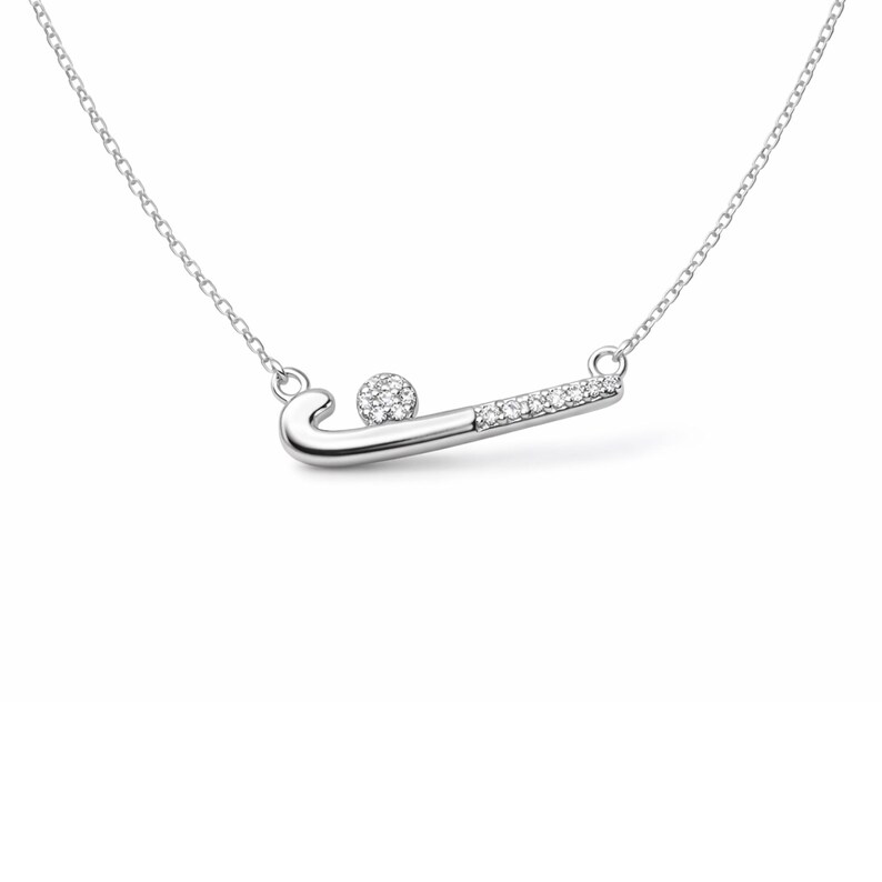 May include: A silver necklace with a hockey stick pendant and a ball. The hockey stick is adorned with small, clear gemstones. The necklace chain is delicate and silver. The pendant is a sports-themed jewellery item.
