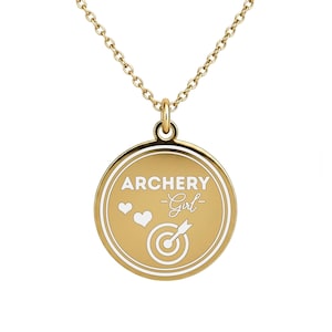 May include: Gold-colored necklace with a round pendant. The pendant features the words "ARCHERY Girl" in white, along with a heart and a target with an arrow. The necklace chain is also gold.