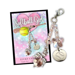 May include: A pink and white sparkly charm with a silver softball charm, a silver angel wing charm, and a silver charm with the word "Loved" on it. The charm is attached to a silver zipper pull. The charm is labeled "Lucky Charm Zipper Pull - Key"