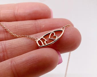 May include: A rose gold-toned necklace featuring a surfboard-shaped pendant with a cutout heart and wave design. The pendant is attached to a delicate, thin metal chain. The metal has a polished finish, reflecting light across its smooth surface.