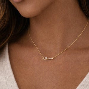 May include: A gold necklace with a horizontal bar pendant. The bar is set with small gemstones and a larger central stone. The necklace is displayed against a skin tone background.