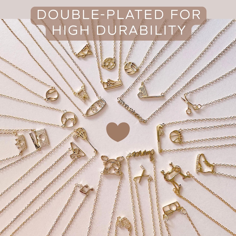 May include: A selection of gold-coloured necklaces with diverse pendant designs, such as sports equipment, scissors, and letters. The image includes the text "DOUBLE-PLATED FOR HIGH DURABILITY". The necklaces are displayed on a white surface.