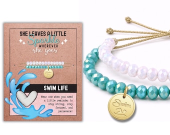 May include: Two beaded bracelets with adjustable gold-tone cords. One bracelet features iridescent white faceted beads, while the other has turquoise faceted beads and a round gold-tone charm engraved with the word Swim and a swimmer icon.