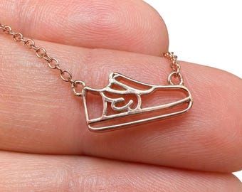 May include: A rose gold-toned necklace featuring a delicate, open-work pendant shaped like a low-top sneaker. The pendant is attached to a thin, matching rose gold-toned chain, creating a minimalist jewelry piece with a clear shoe silhouette.