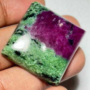Op de afbeelding: Een groene en roze edelsteen cabochon met een vierkante vorm. De edelsteen heeft een gevlekt patroon van groen en roze.